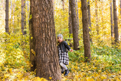 Woman standing by tree trunk in forest during autumn