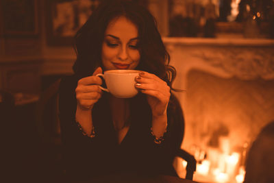 Smiling beautiful woman sipping fresh coffee in cafe closeup over burning candles. good evening