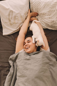 A happy teenage girl is playing kissing having fun with her pet a small dog in a bed in a cozy house