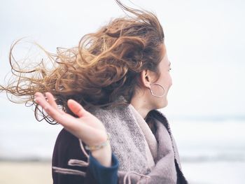 Portrait of woman with arms raised on beach against sky