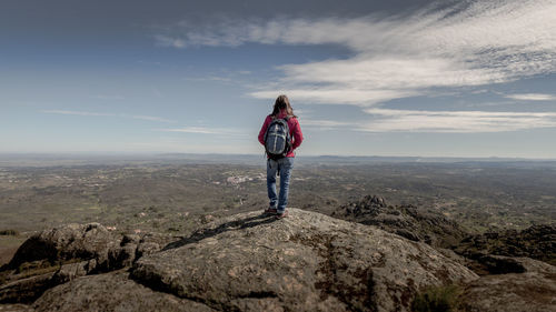 Rear view of hiker standing on rock by landscape against sky