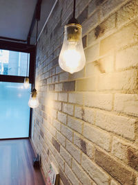 Low angle view of illuminated light bulb hanging on wall