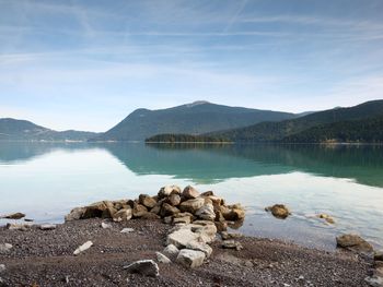 Big boulders sticking out from smooth lake water level. green blue water, mountain in water mirror.