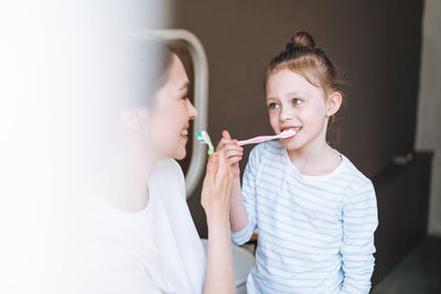 Young mother woman with little tween girl daughter in pajamas brushing teeth in the morning at home