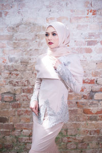 Young woman standing against brick wall