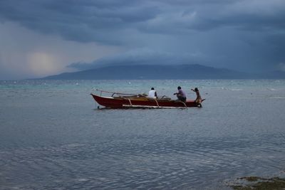 People on boat at beach against sky