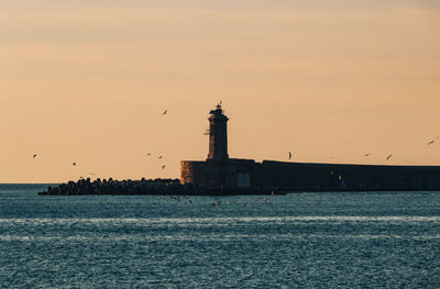 Lighthouse by sea against sky during sunset