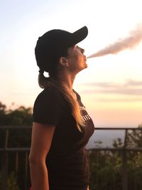 Side view of woman smoking while looking away against sky during sunset