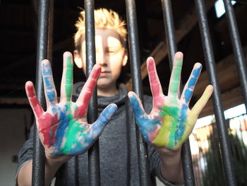 Portrait of teenage boy showing painted hands behind fence