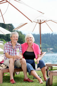 Portrait of senior couple sitting against lake at resort