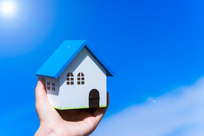 Cropped image of hand holding model home against blue sky