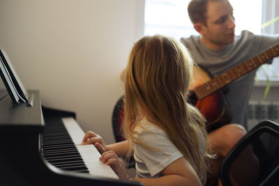Girl playing piano while sitting with father at home