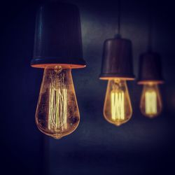 Close-up of illuminated light bulb hanging in the dark
