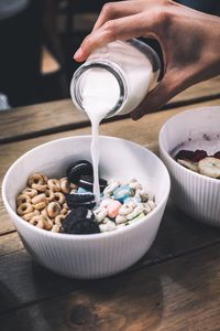 Close-up of hand pouring milk in granola bowl at table