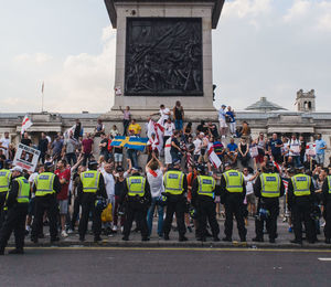 People and police force standing on street in city against sky