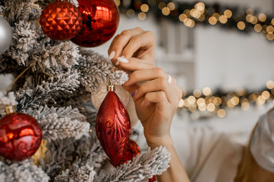 Close up of beautiful woman hands decorating new year tree with christmas lights as a background