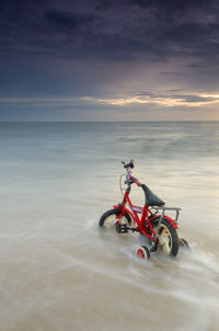 Man riding motorcycle on beach against sky during sunset