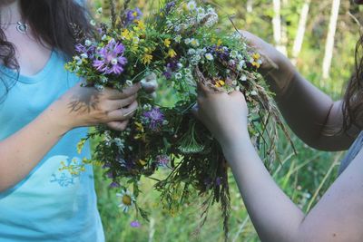 Cropped image of woman making wreath with female friends in yard