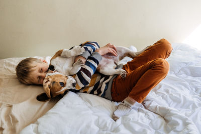 Full length of boy lying down with dog on bed