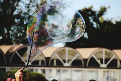 Close-up of hand holding bubbles against sky