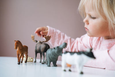 Little girl toddler in pink playing with animal toys on table in children's room at home