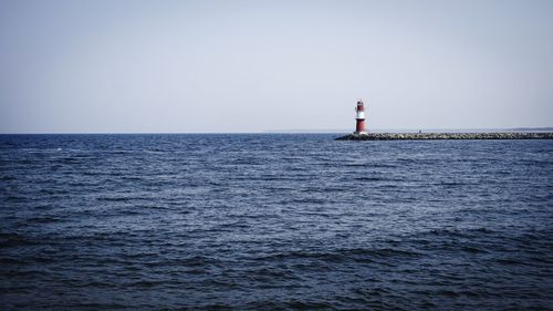 Lighthouse by sea against clear sky