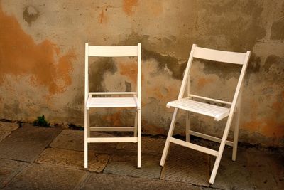 Empty chairs on footpath against wall