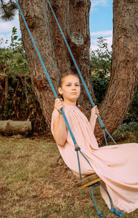 Girl sitting on swing against tree trunk