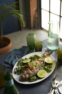 Roasted whole fish dish in a table setting with glasses and napkin