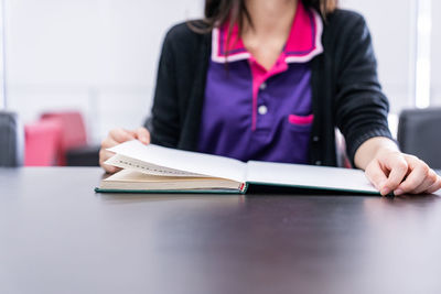 Midsection of woman reading book on table