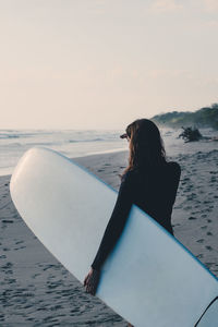 Mature woman carrying surfboard at beach during sunset