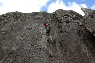 Low angle view of man climbing on rock against sky