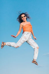 Portrait of young woman jumping against blue sky