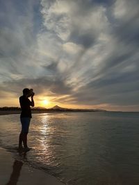 Woman standing on beach against sky during sunset