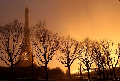 Low angle view of silhouette trees by eiffel tower against sky during sunset