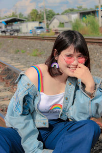 Portrait of smiling young woman wearing sunglasses sitting on railroad track