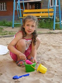 Cute girl crouching while playing in sand at playground