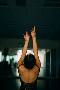 Rear view of woman with hands raised at dance studio