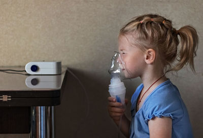 Little girl makes inhalation with a nebulizer at home, sitting on a chair. 