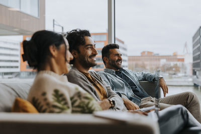 Happy male and female colleagues sitting on sofa in conference meeting