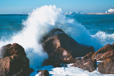 Waves splashing on rocks at shore against sky