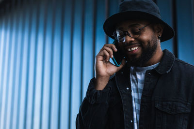 Young man using mobile phone while standing against wall