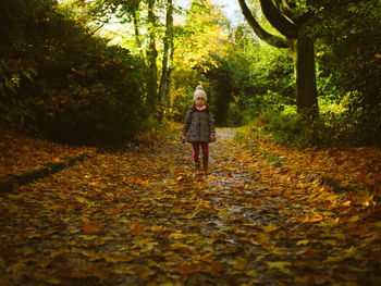 Full length of young girl standing amidst leaves in forest