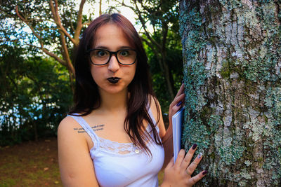 Portrait of young woman making face while standing by tree