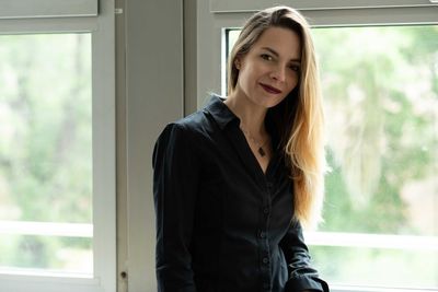 Portrait of beautiful young woman standing against window