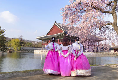 Rear view of woman with pink umbrella by lake against sky