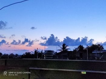 Silhouette trees by field against sky during sunset