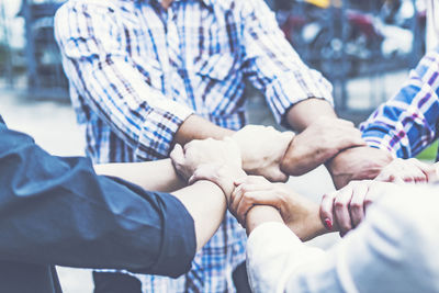 Close-up of friends holding hands while huddling outdoors