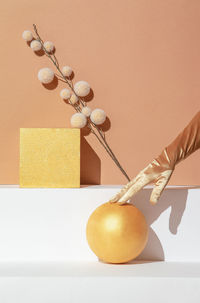 Autumn minimalistic scene, hand in golden gloves, decor cube, ball and dry brunch in styish beige 
