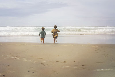 Rear view of siblings running at beach